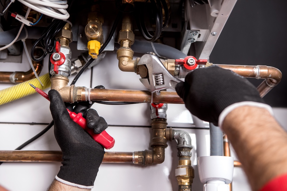 Plumber using tools to adjust copper pipes during a heating system repair